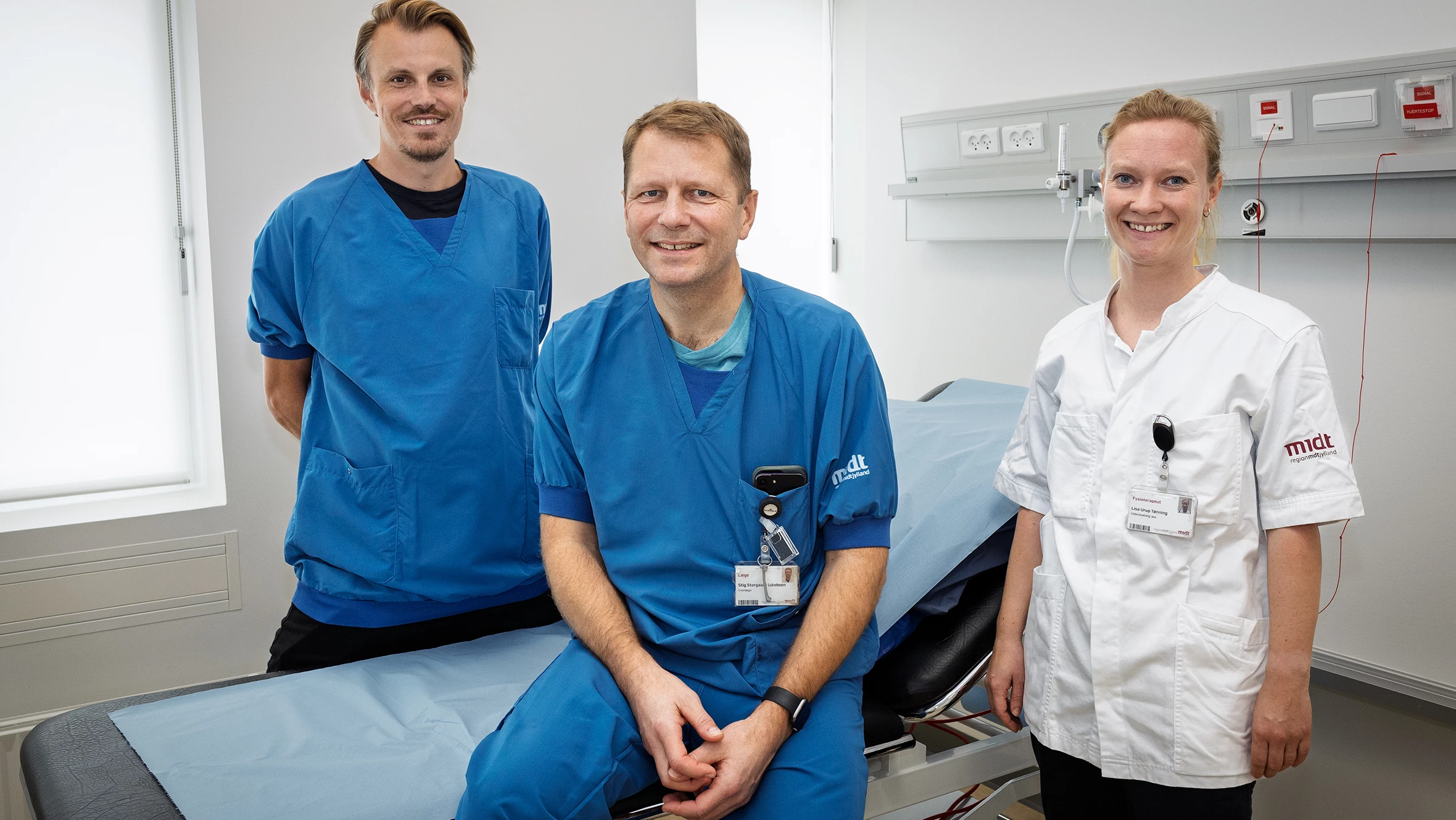 To læger og en fysioterapeut fotograferet i et undersøgelsesrum.