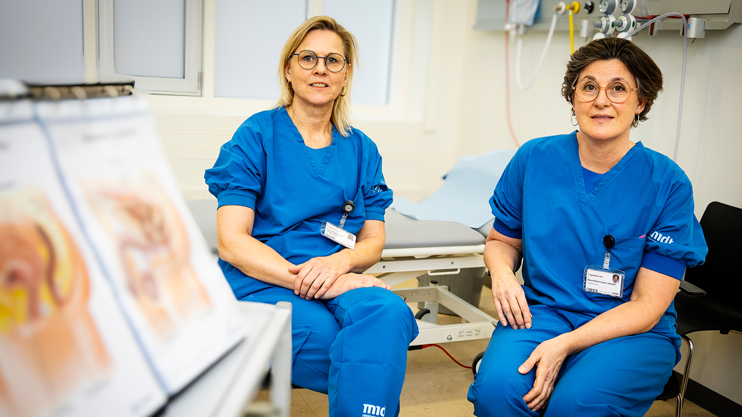 To sygeplejersker i blå arbejdsuniform.